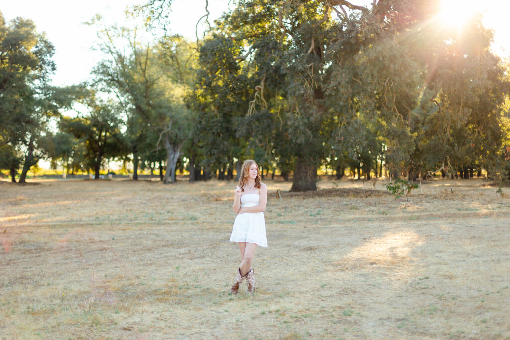 a woman in a white dress standing in a field with trees, posing for photography that will be used in blogging.