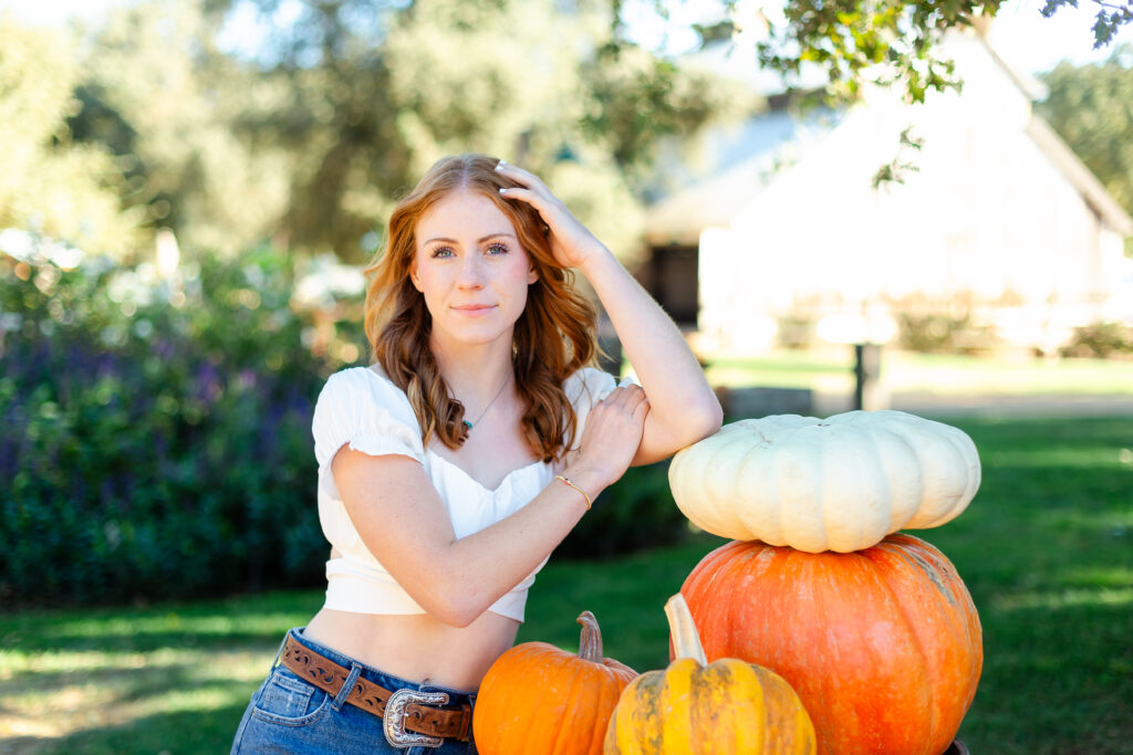 a high school senior posing with a stack of pumpkins for images that will be used for blogging.
